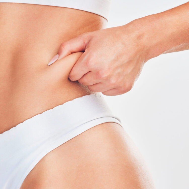 Hand, pinch and woman in underwear her belly fat for weight loss on a white studio background. Overweight, cellulite and fat with a woman with a healthy lifestyle and diet for stomach loss.